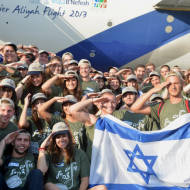 New immigrants from USA and Canada salute and hold up Israeli flags as they arrive in a special "Soldier Aliyah Flight